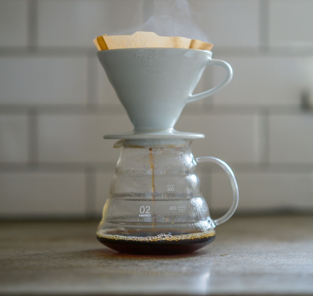 Hario V60 process with a white ceramic filter and glass carafe on a countertop.
