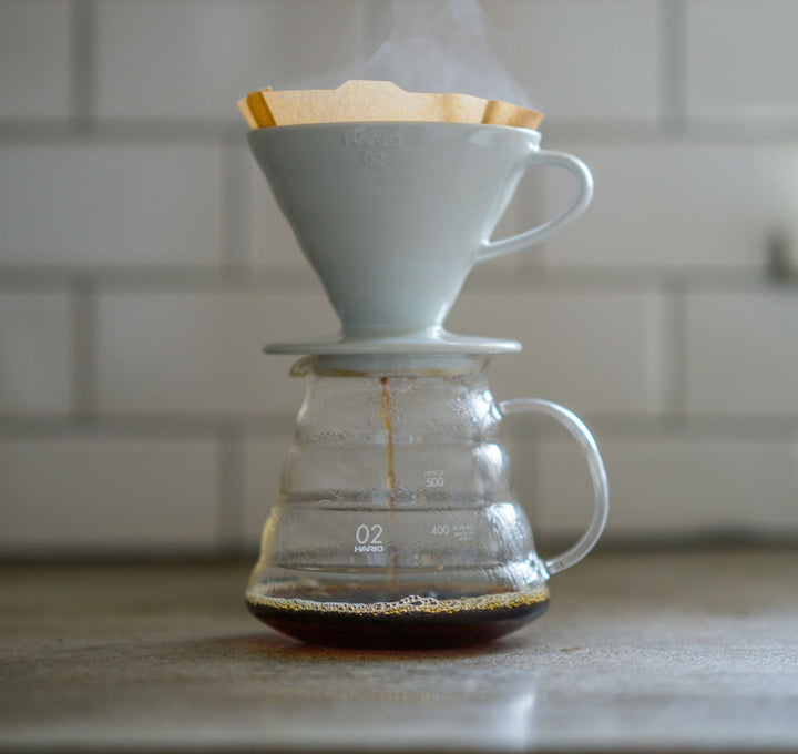Hario V60 process with a white ceramic filter and glass carafe on a countertop.