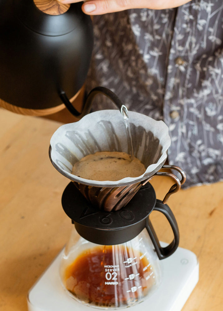 Person making coffee using a pour-over coffee maker on a wooden surface