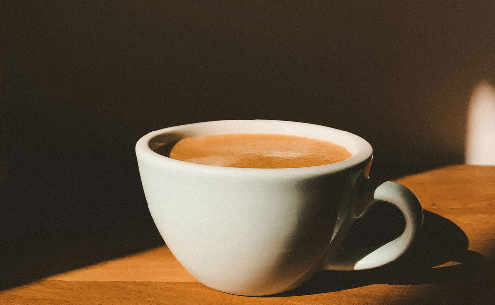White cup of coffee on a wooden table with a dark background