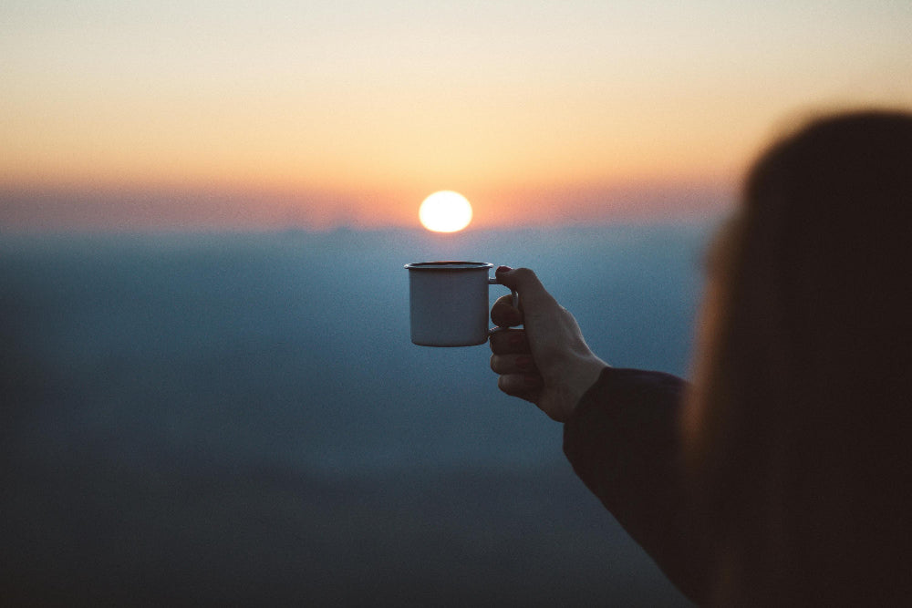Person holding a cup of coffee with a sunset in the background